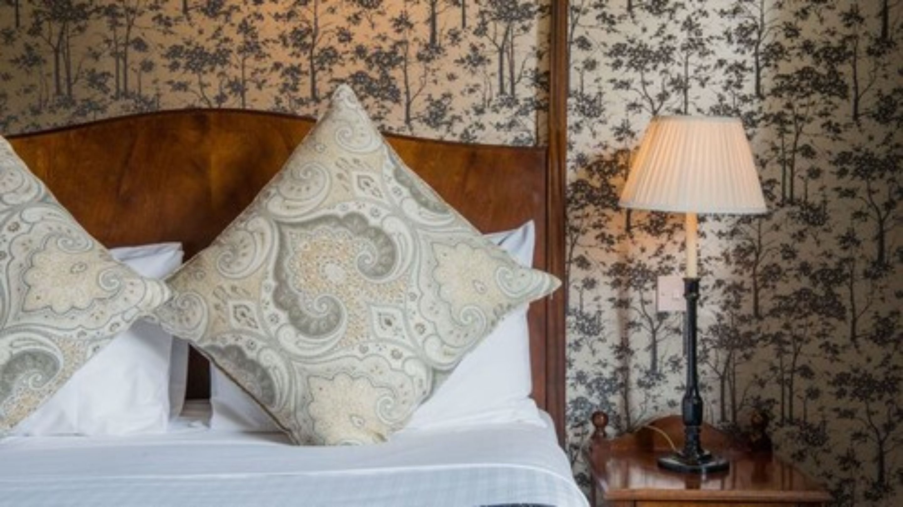 A neatly made bed with patterned pillows, a wooden headboard, and a nightstand with a lamp.