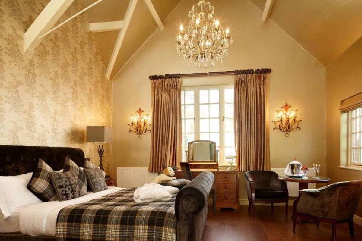 A spacious bedroom with a large bed, a chandelier, and a desk with a chair.