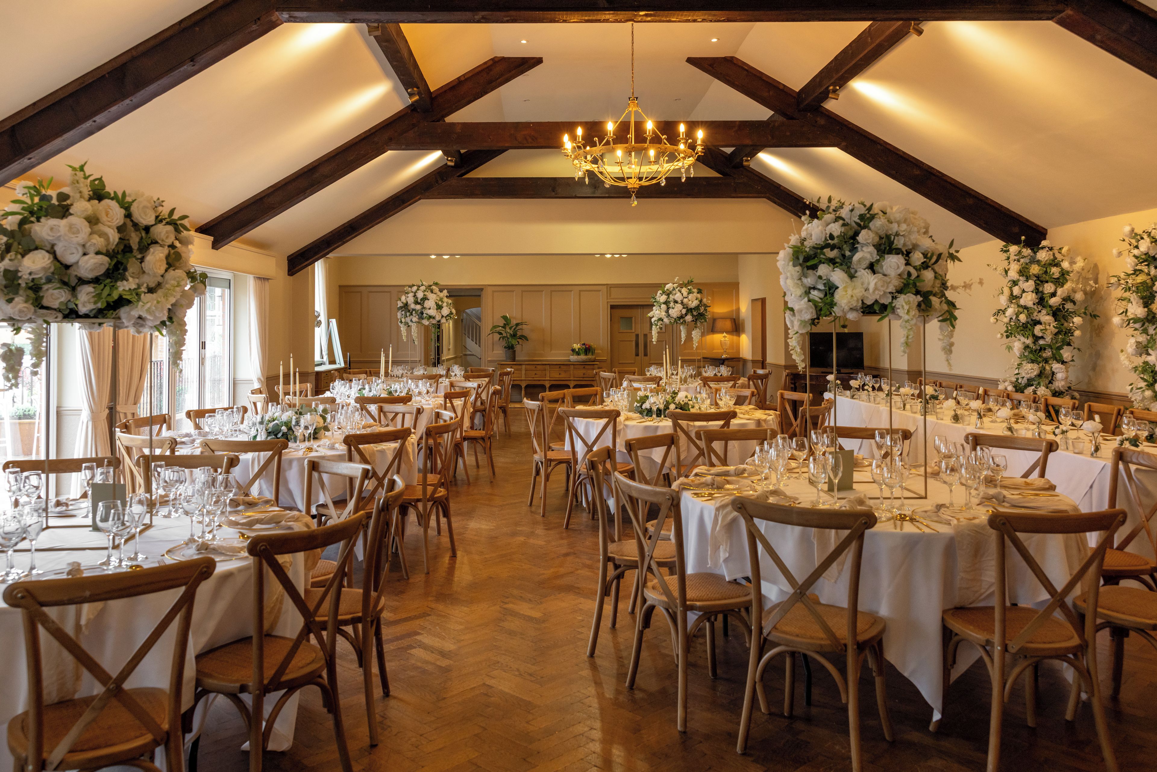 A banquet hall with multiple tables set for dining, wooden chairs, and a chandelier.