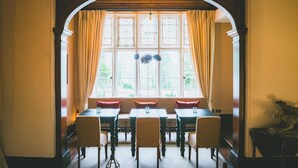 Ein Essbereich mit einem langen Tisch, Stühlen, einer gepolsterten Bank und einem großen Fenster mit Vorhängen.