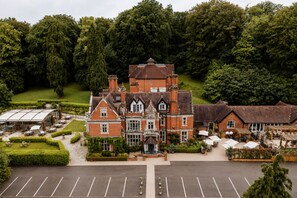 A large, historic building with multiple wings, surrounded by lush greenery and a parking lot. - The Coed-Y-Mwstwr Hotel (Bridgend)