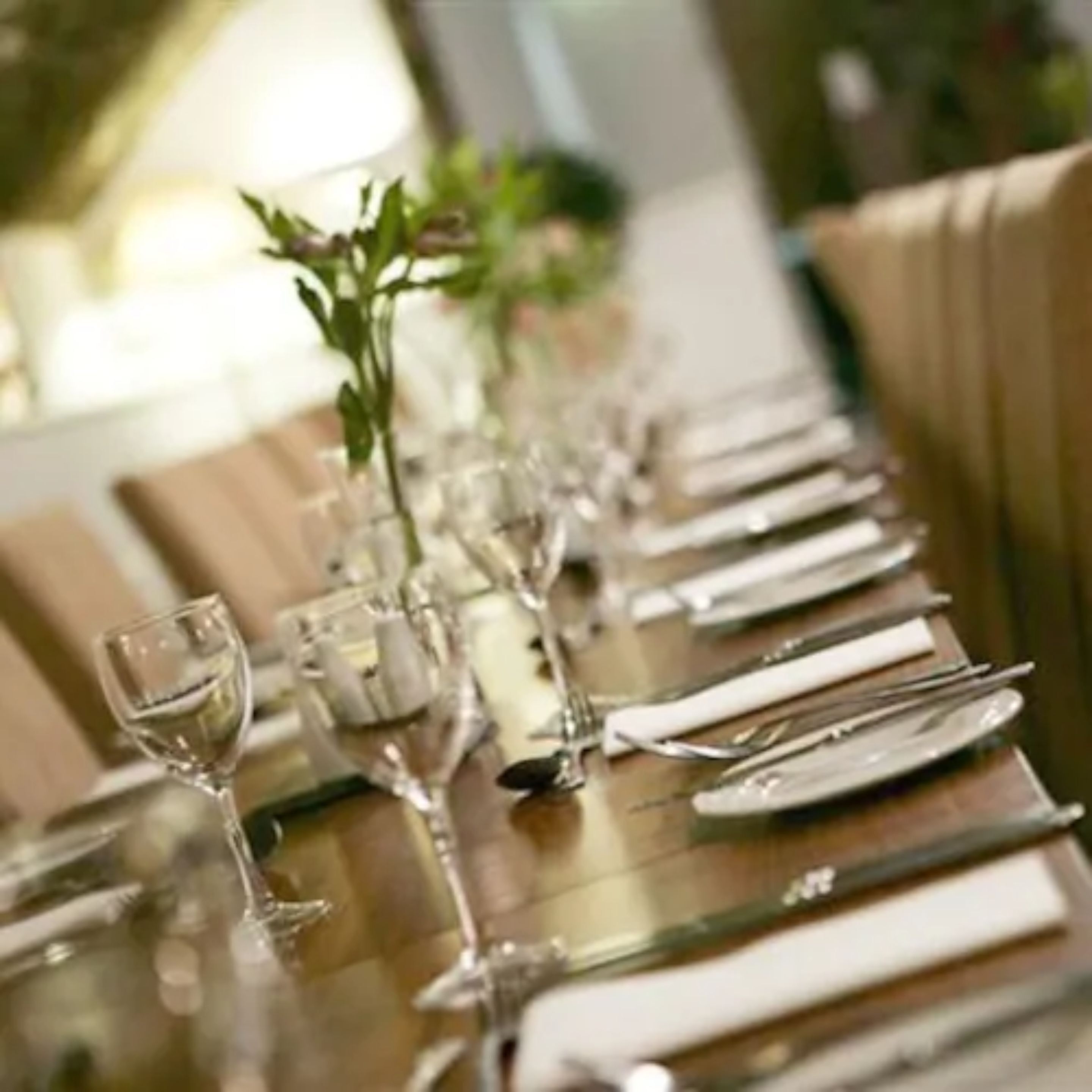 A long dining table set with multiple place settings, including plates, cutlery, and glasses.