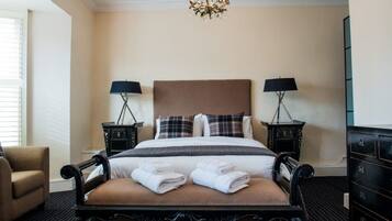 A hotel room with a large bed, two bedside tables with lamps, a chandelier, a chair, and a dresser.