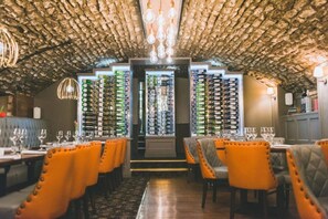 Ein Restaurant mit rustikalem Deckenbau, mehreren Esstischen mit orangefarbenen Stühlen und einer Weinstraße an der Wand.