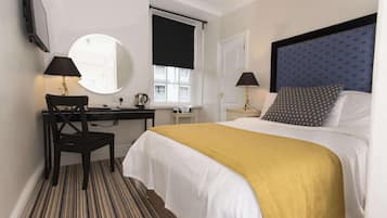 Hotelkamer met een bed, een bureau, een stoel, een spiegel, een raam met een donkerblauw zonnescherm en een aan de muur bevestigde televisie.