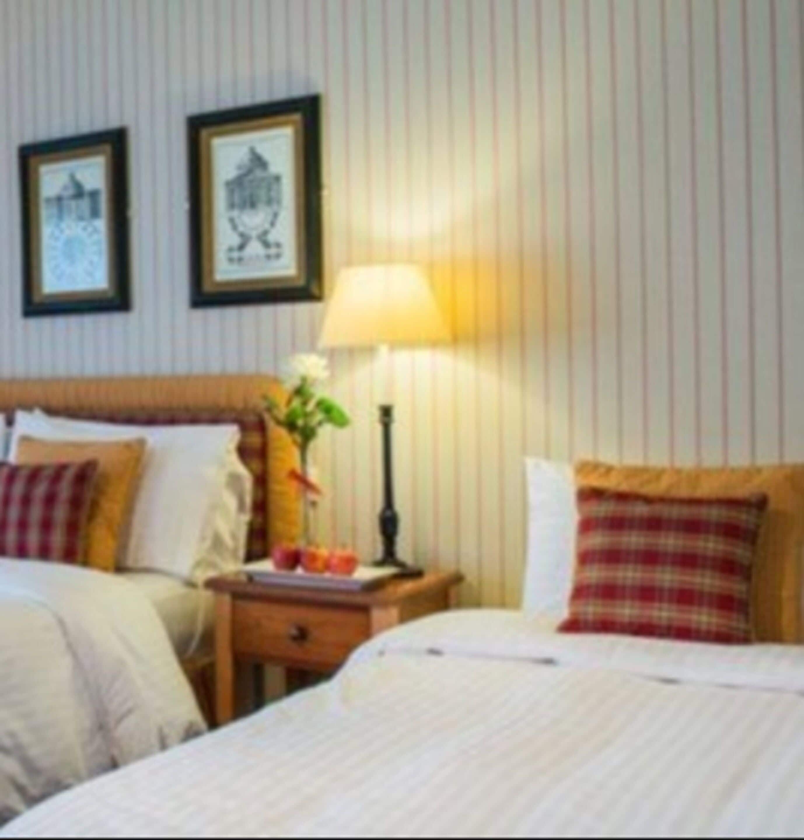 A hotel room with two beds, a nightstand with a lamp, and framed pictures on the wall.