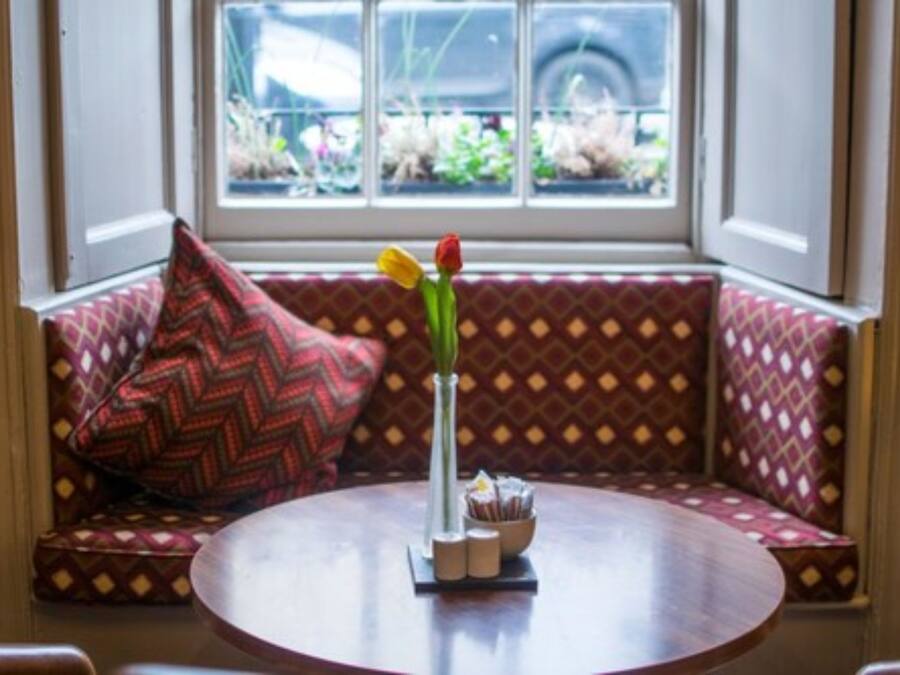 Un coin salon confortable avec des coussins à motifs et une table ronde agrémentée d’un vase de fleurs.