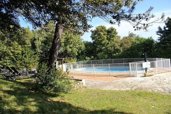 A swimming pool surrounded by a white fence, with lounge chairs and a stone deck in the foreground. - Le Logis Du Chateau (Vaison-la-Romaine)