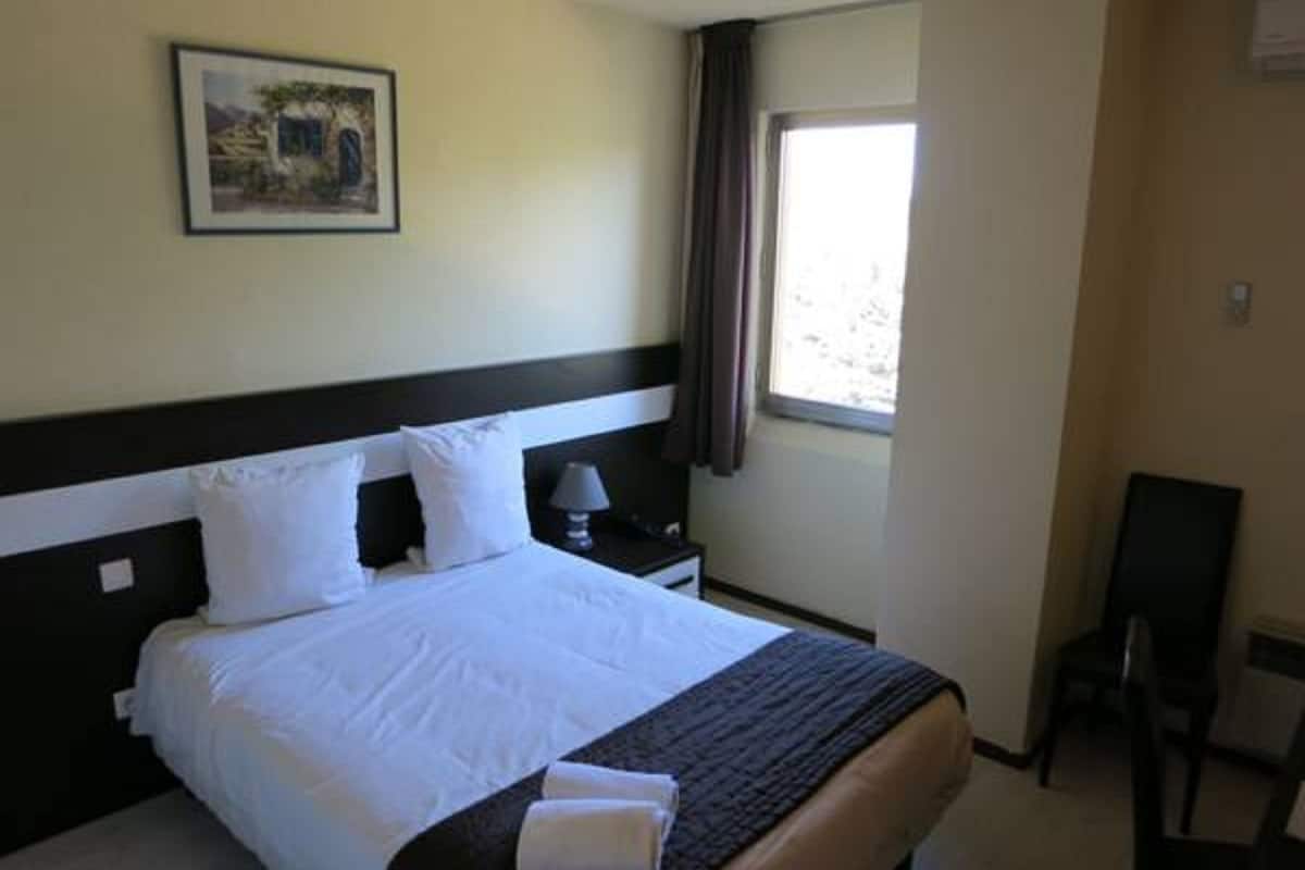 Une chambre d’hôtel avec un grand lit, une table de chevet avec une lampe, une fenêtre avec des rideaux et une chaise.