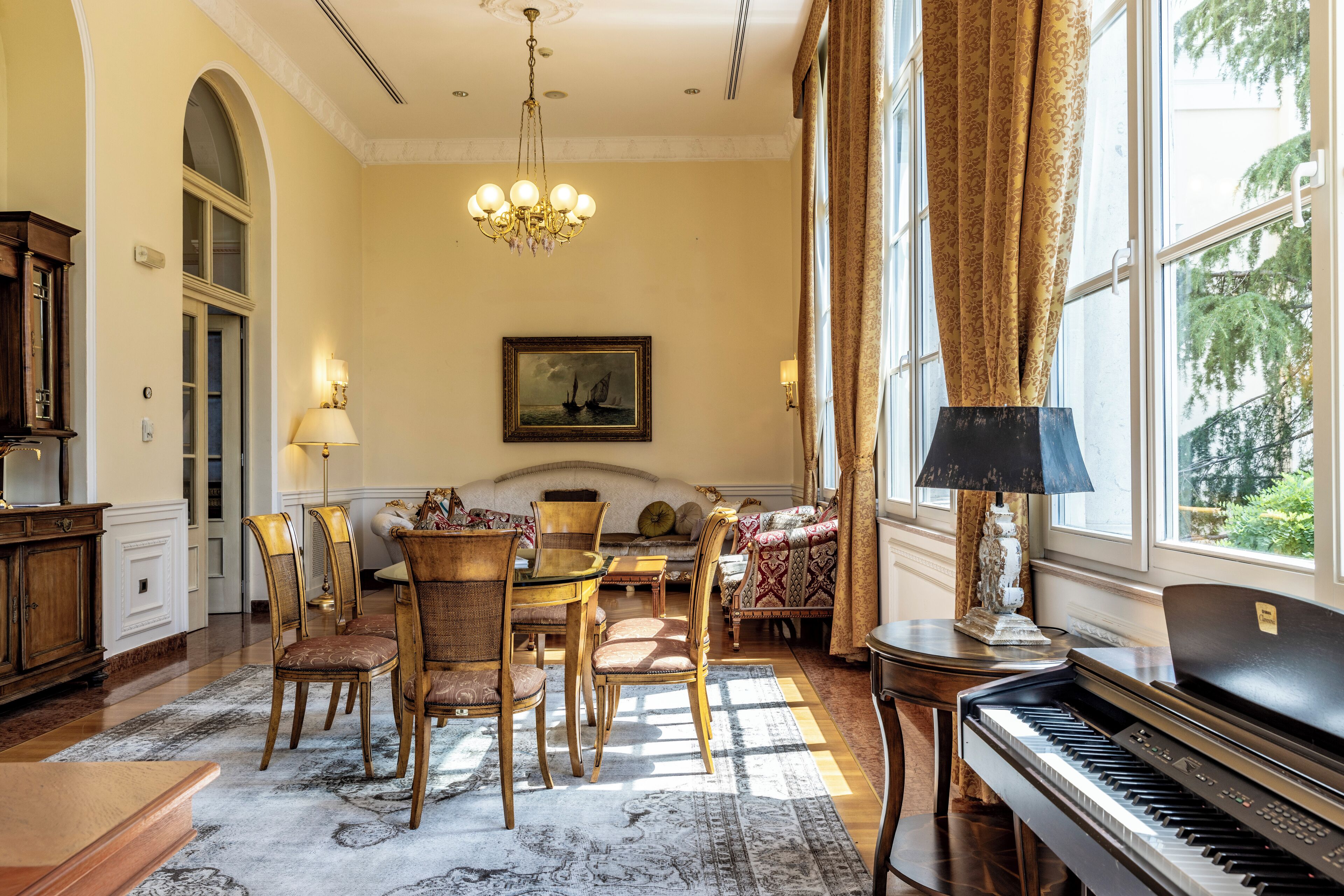 A spacious living room with a piano, a dining area with chairs and a table, and a large window with curtains.