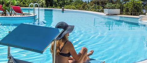 En kvinna sitter i en solstol vid en pool med utsikt över havet.