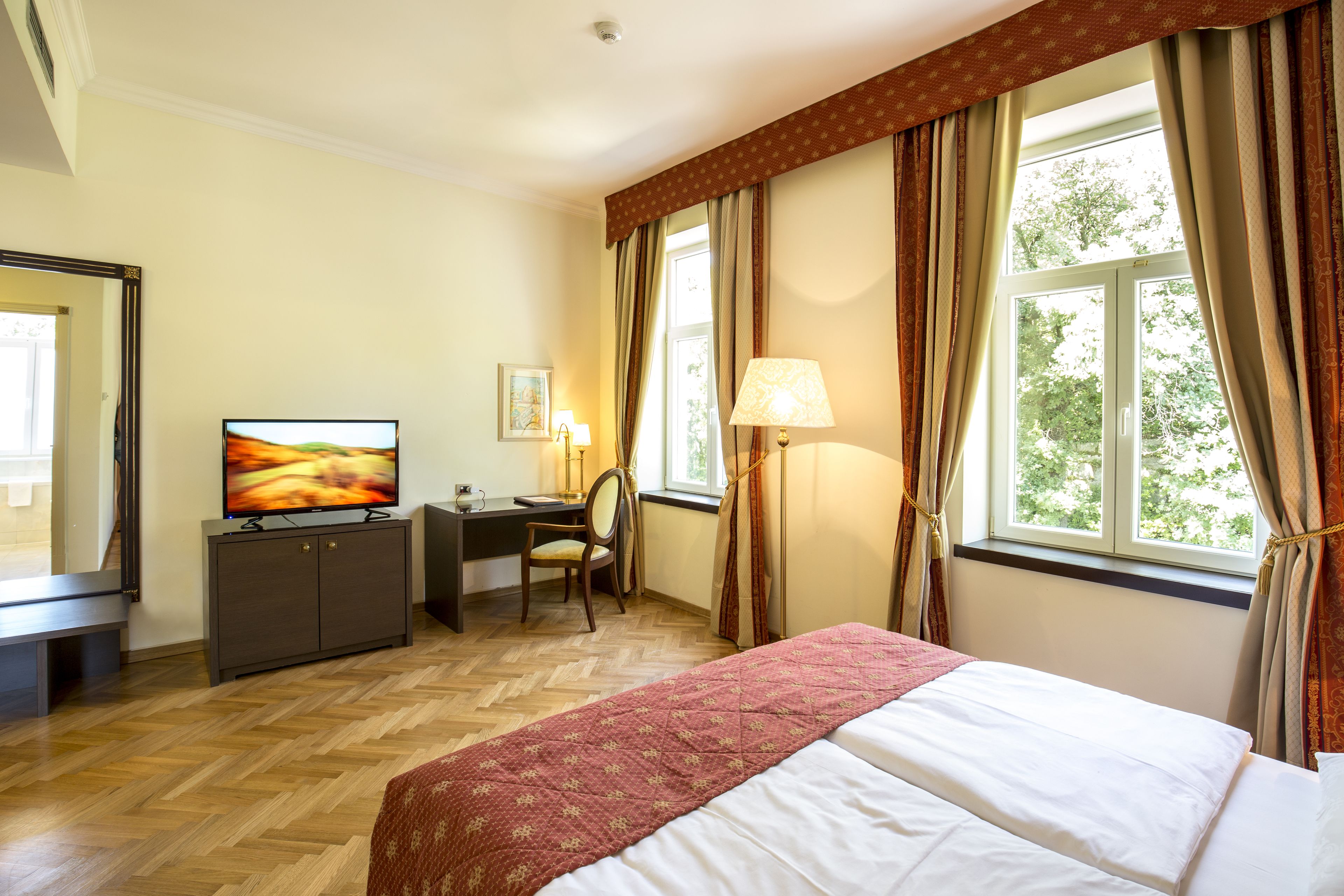 A hotel room with a bed, a desk, a chair, a television, and a window with curtains.