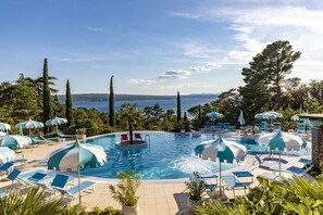 Zona de piscina con sillones de descanso y sombrillas, rodeada de árboles y vista al mar.