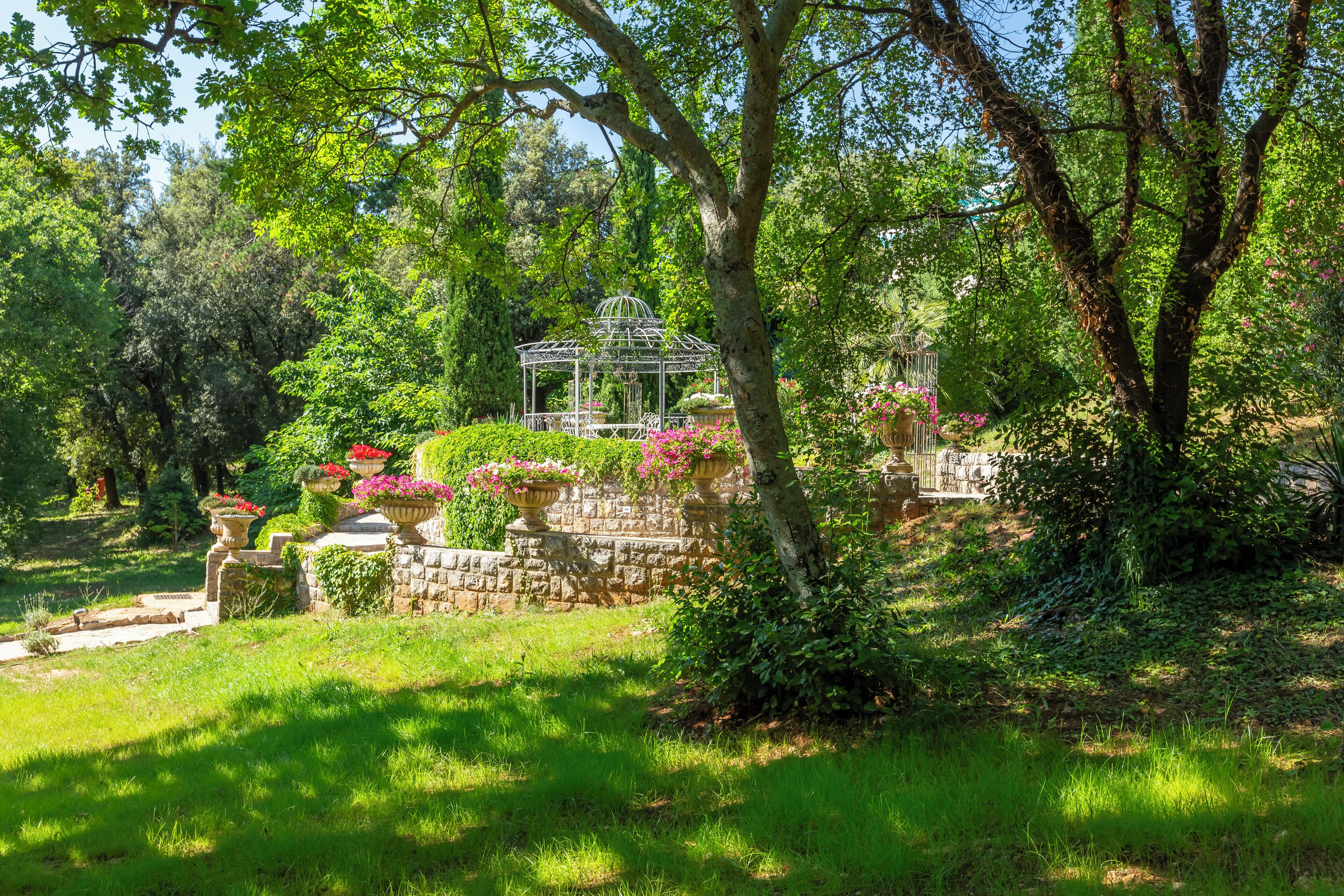 A garden with a gazebo, stone walls, and various plants.