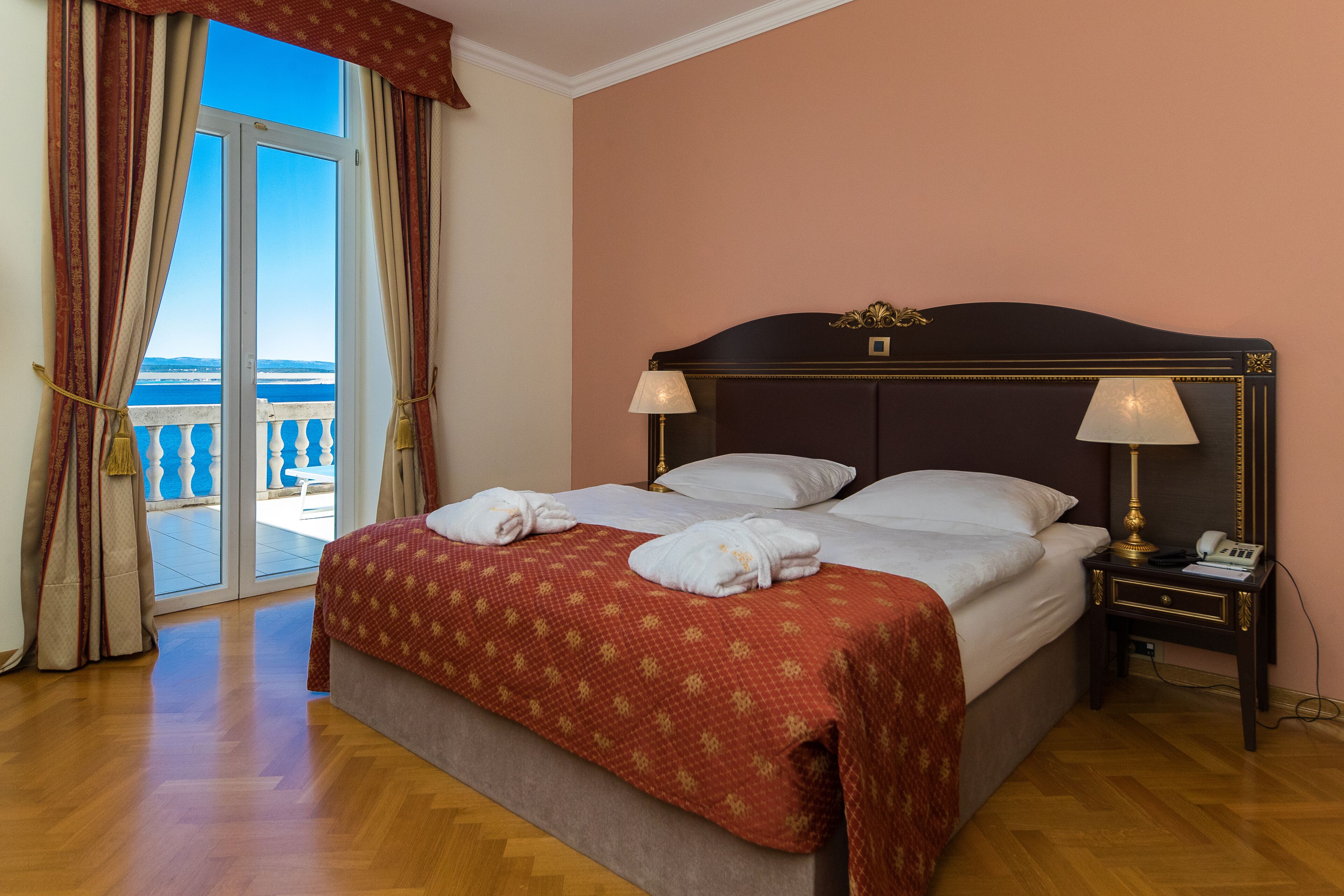 Habitación de hotel con cama, dos lámparas de noche, una mesita de noche y vista al mar a través de un ventanal corredero.