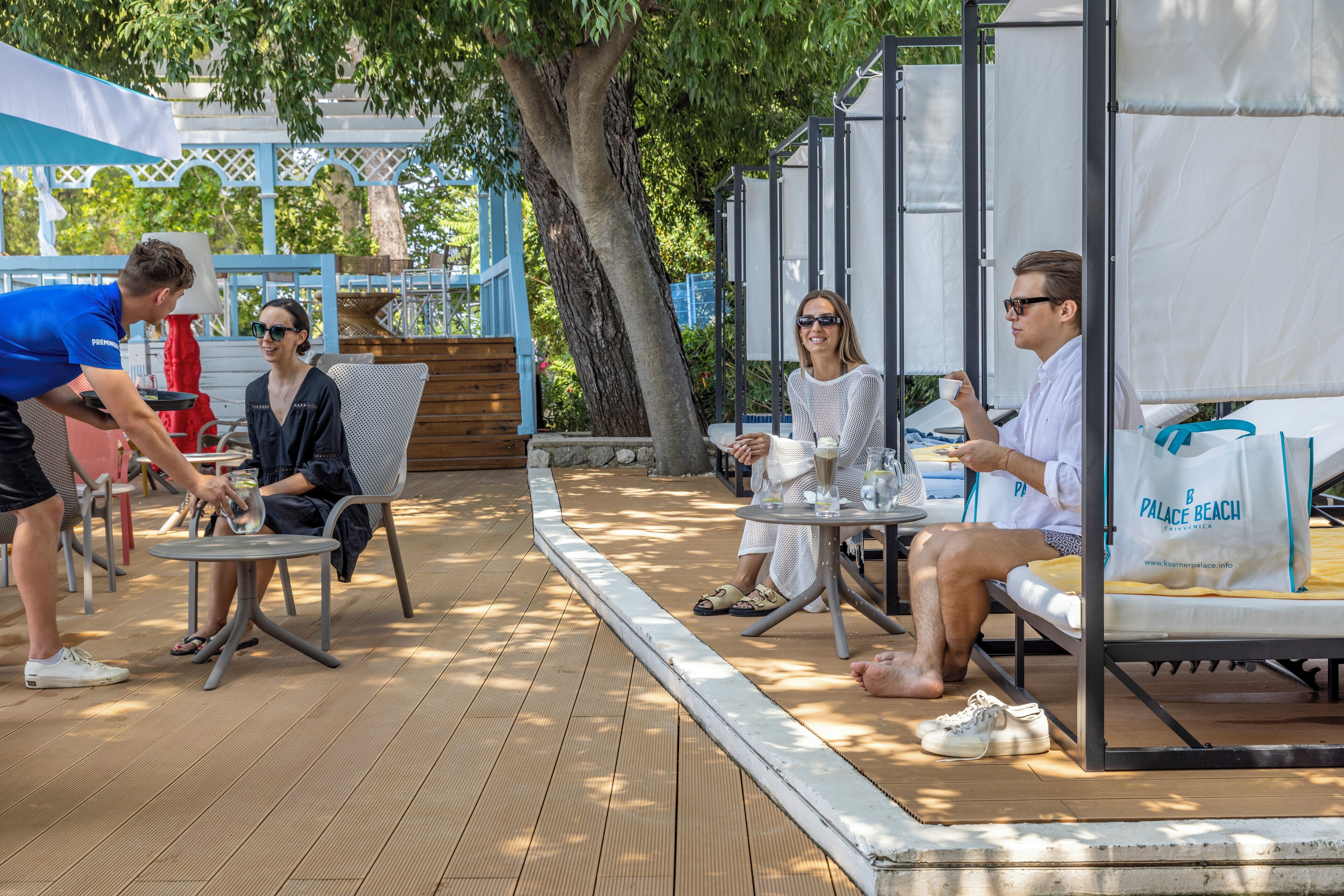 An outdoor seating area with tables and chairs, a wooden deck, and a tree providing shade.