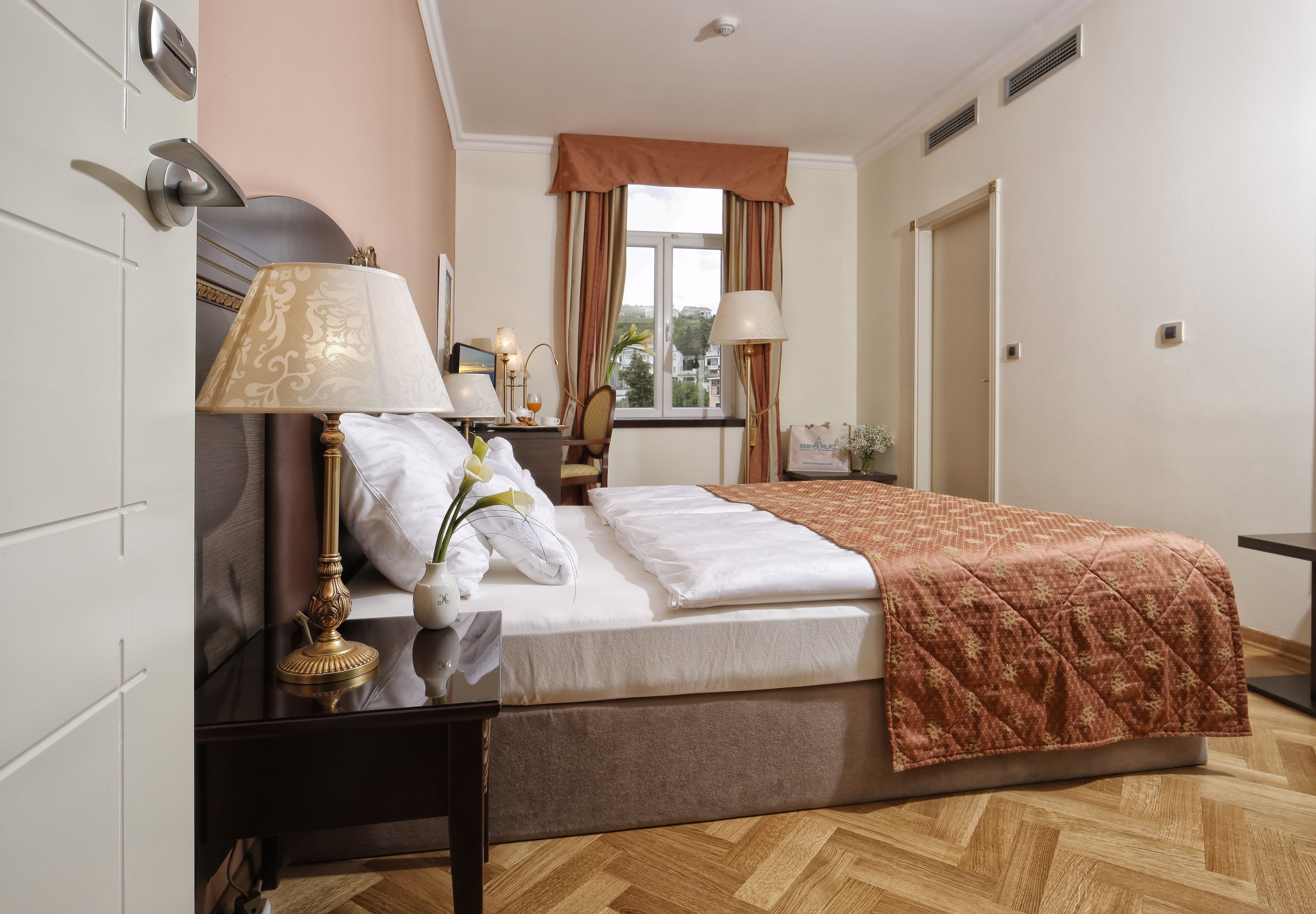 A neatly arranged bedroom with a bed, bedside tables, lamps, and a window with curtains.