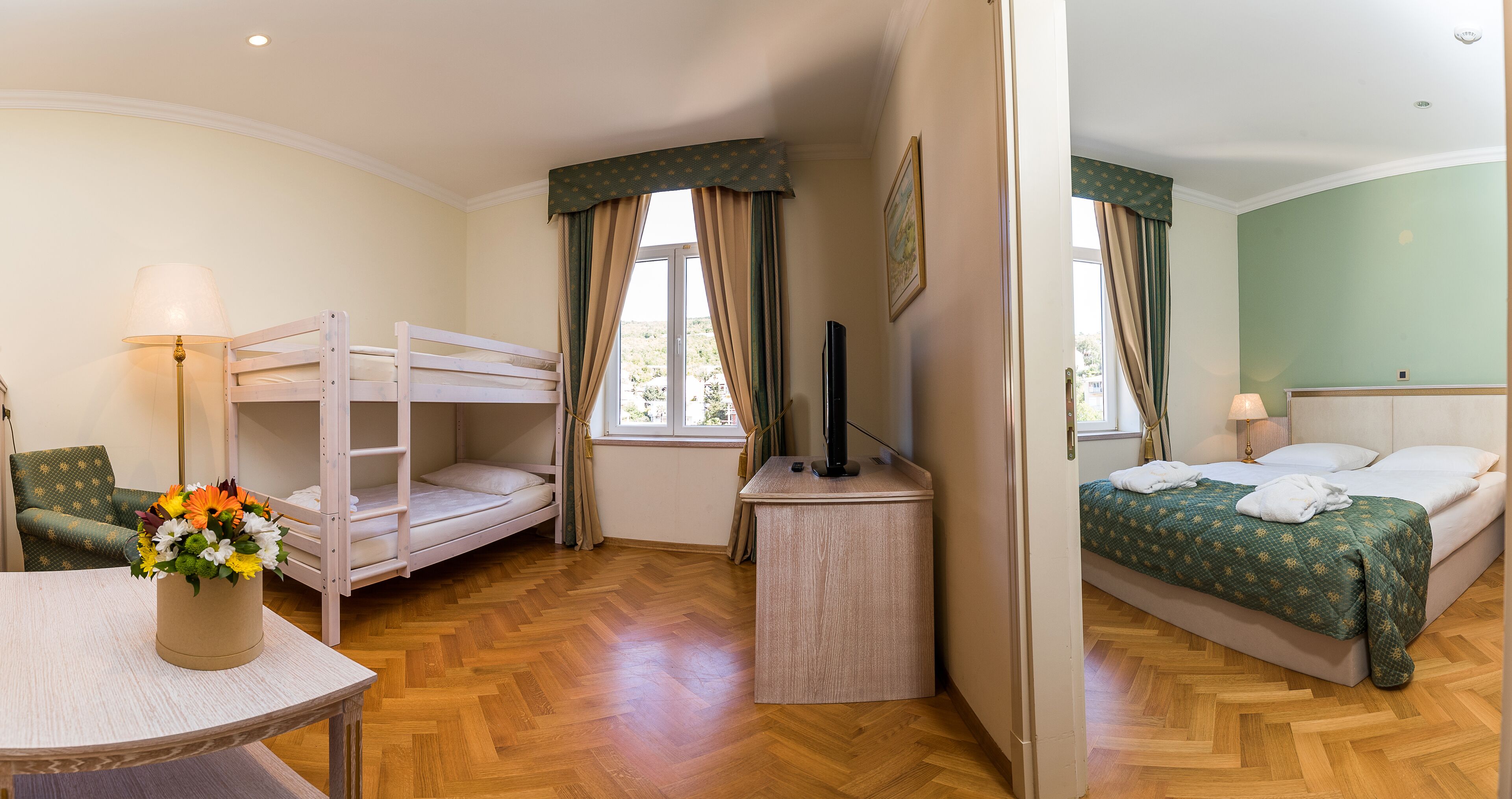 Una habitación con literas, un escritorio, una silla, una mesa con un jarrón de flores y una cama con una manta verde.