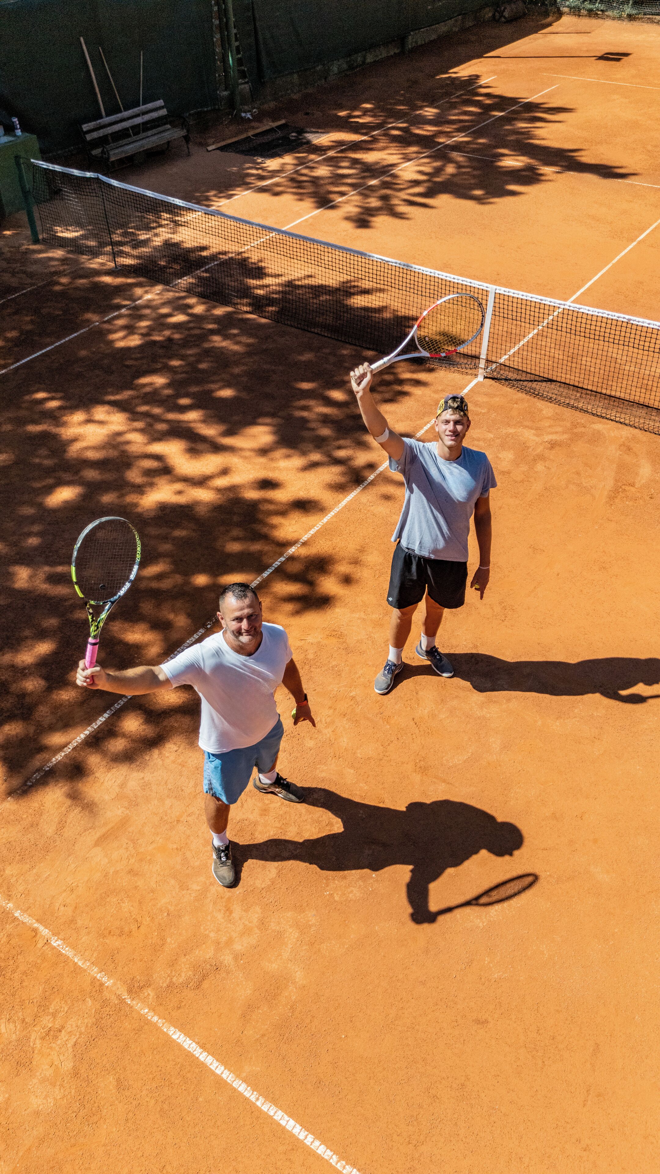 A tennis court with two players, one holding a racket raised in victory.
