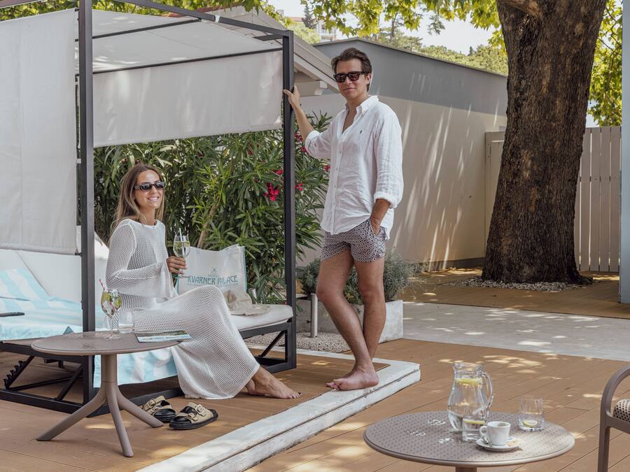 Ein überdachter Außenbereich mit Tisch, Stühlen, einer Pergola und einem Baum.