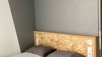 A bed with a wooden headboard, two pillows, and a white mattress in a room with gray walls and a sloped ceiling.