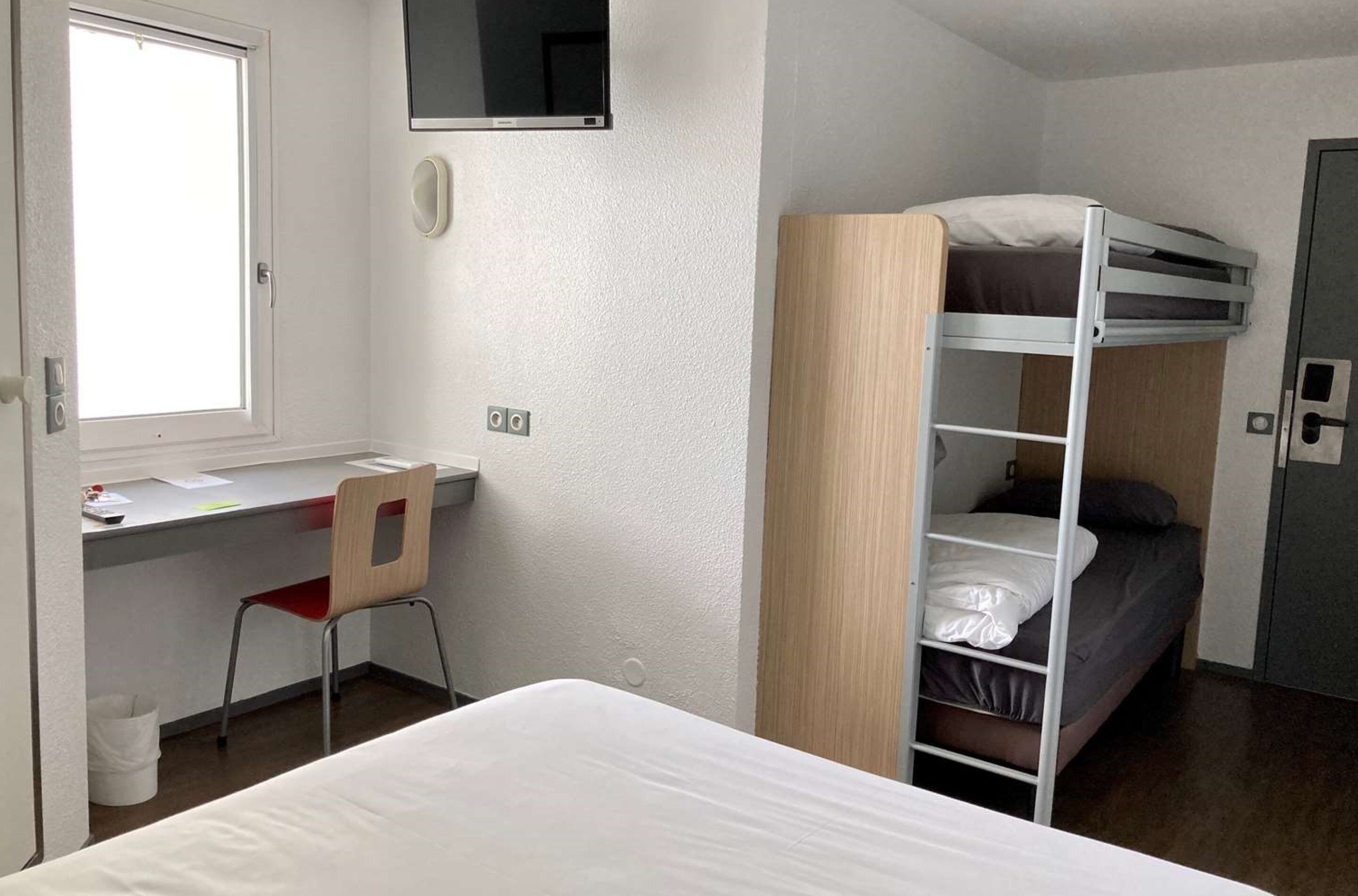 Une petite pièce comprenant un lit superposé, un bureau avec une chaise, une fenêtre et une porte.