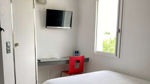 Une chambre à coucher avec un lit, un bureau et une chaise, une télévision et une fenêtre.