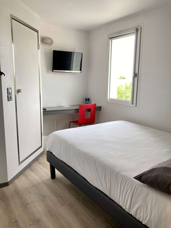 Un dormitorio con una cama, un escritorio con silla, un televisor y una ventana.