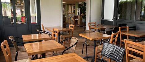 A cafe interior with wooden tables and chairs, a green door, and a view through large windows.