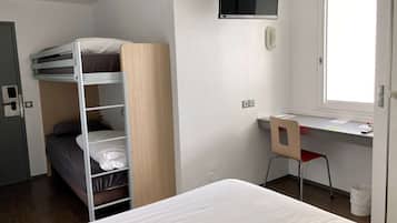 Una cama individual superpuesta, un escritorio con silla, un televisor y una ventana en una habitación de hotel.