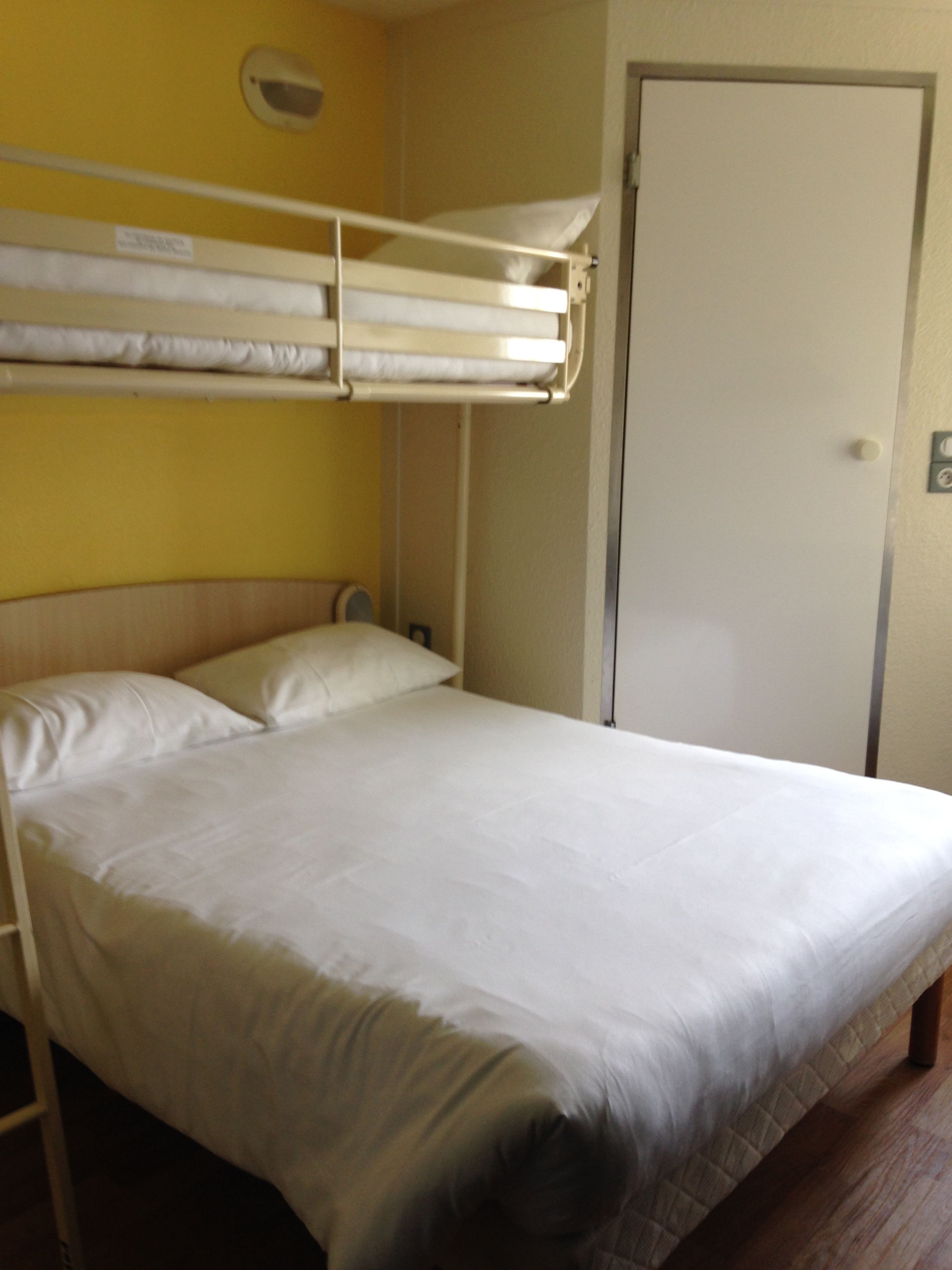 A bunk bed with white bedding in a room with yellow walls and a white door.