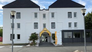 Un bâtiment à deux étages doté d’une façade symétrique, d’une entrée centrale surmontée d’une arche jaune et d’un parking situé à l’avant.