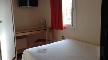 Ein Hotelzimmer mit Bett, Schreibtisch, Sessel, Fernseher und einem Fenster mit roten Vorhängen.
