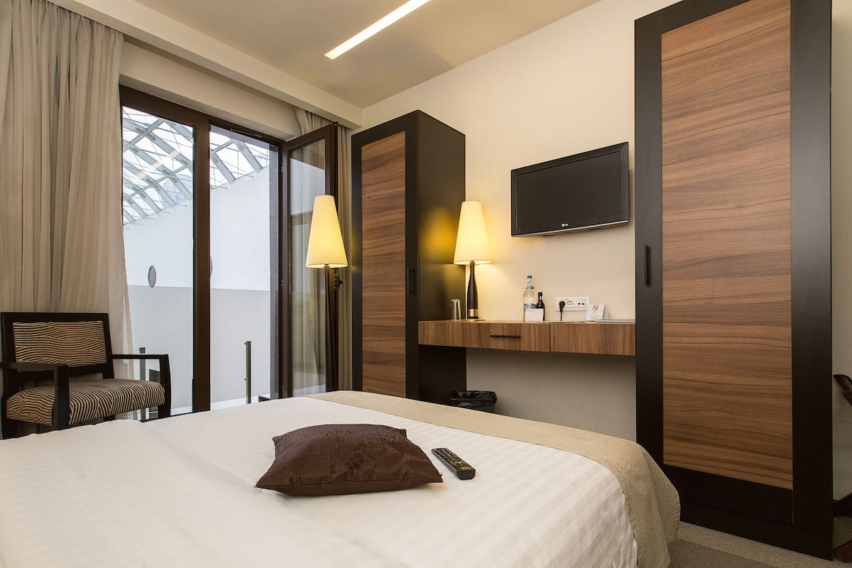 Hotellihuone, jossa on sänky, tuoli, televisio ja ikkuna, jossa on verhot.