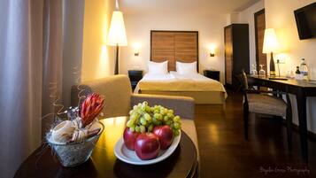 A hotel room with a bed, bedside tables, a desk, and a dining table with a fruit bowl.