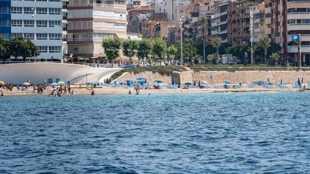 A beach with a row of blue umbrellas and a sandy shore. - Hotel Golden (Benidorm)