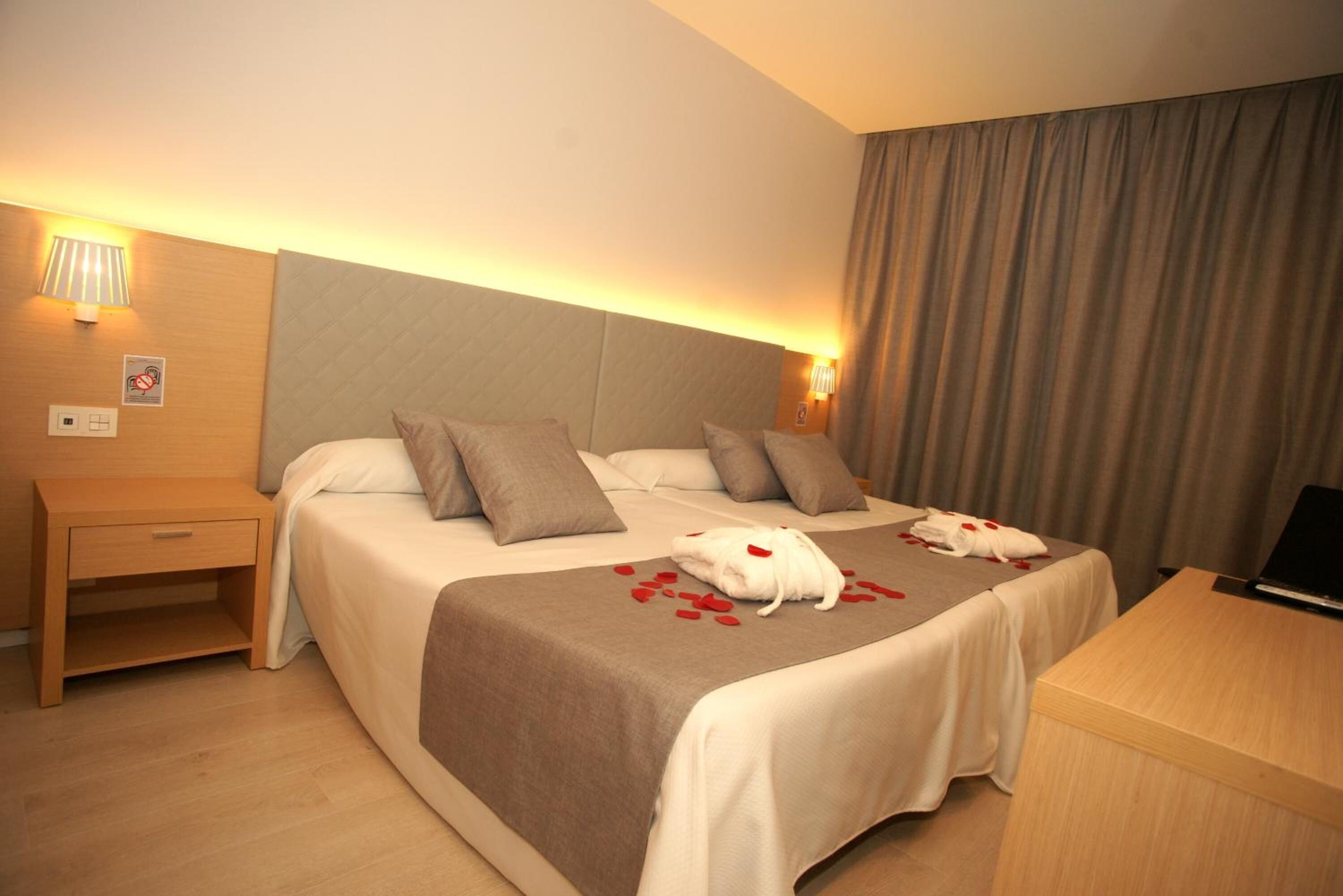 Una habitación de hotel con cama, mesitas de noche, un escritorio y una lámpara.