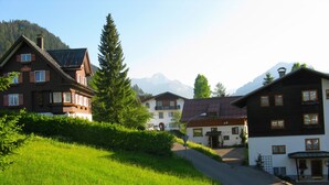 A row of traditional European-style buildings with sloped roofs, set against a backdrop of mountains.