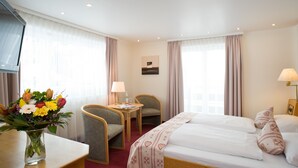 A hotel room with a bed, a desk, a chair, a table, and a vase of flowers.