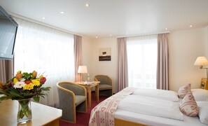 A hotel room with a bed, a desk, a chair, a table, and a vase of flowers. - Riezler Hof (Mittelberg)