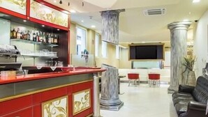 Una zona de bar con una barra roja, un área de estar con un sofá y sillas, y una pantalla grande al fondo.