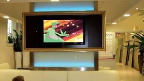 Un televisor montado en una pared en el vestíbulo de un hotel, con un sofá blanco al frente.