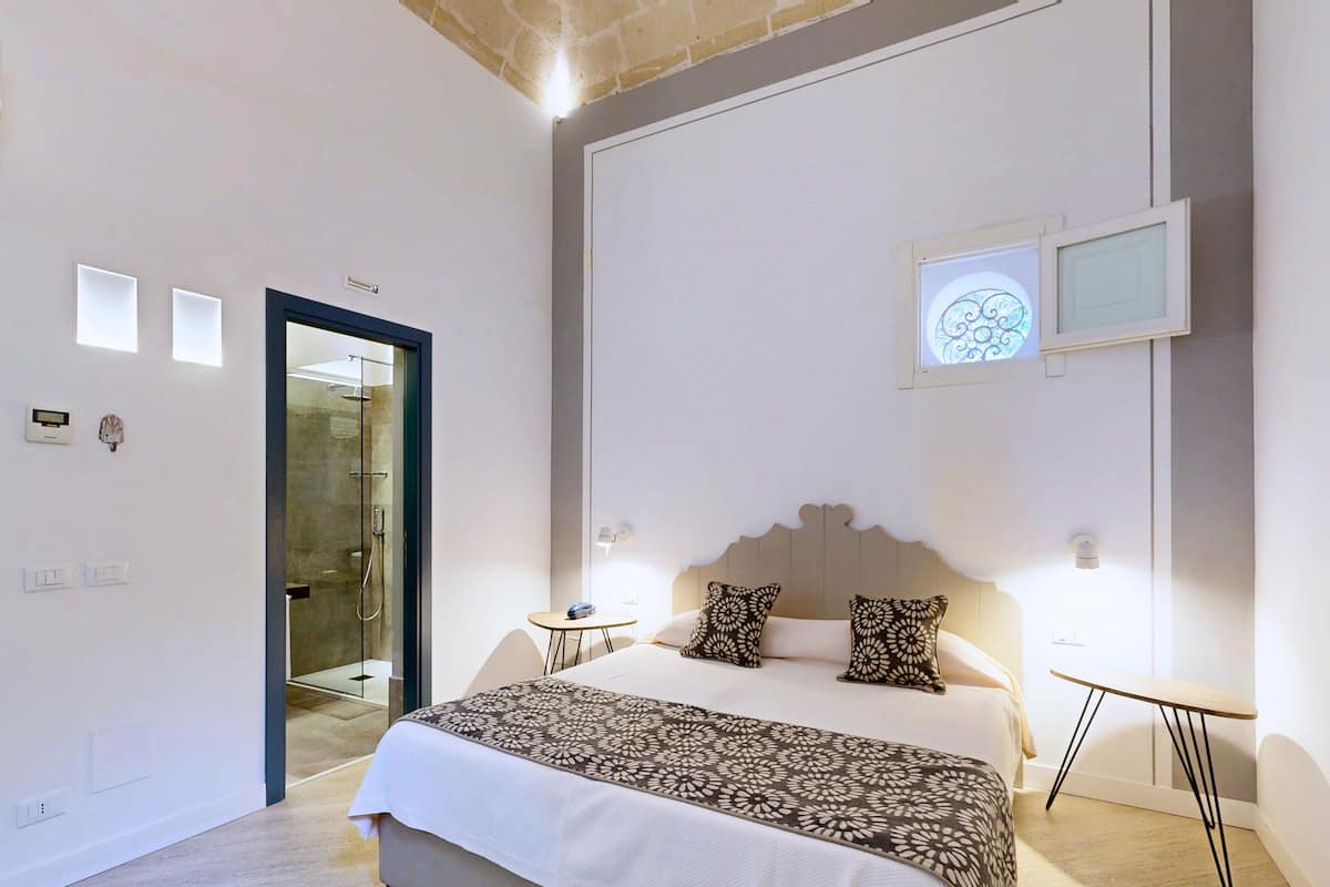 Una habitación de hotel moderna con una cama grande, mesitas de noche, una pequeña mesa redonda y zona de ducha.