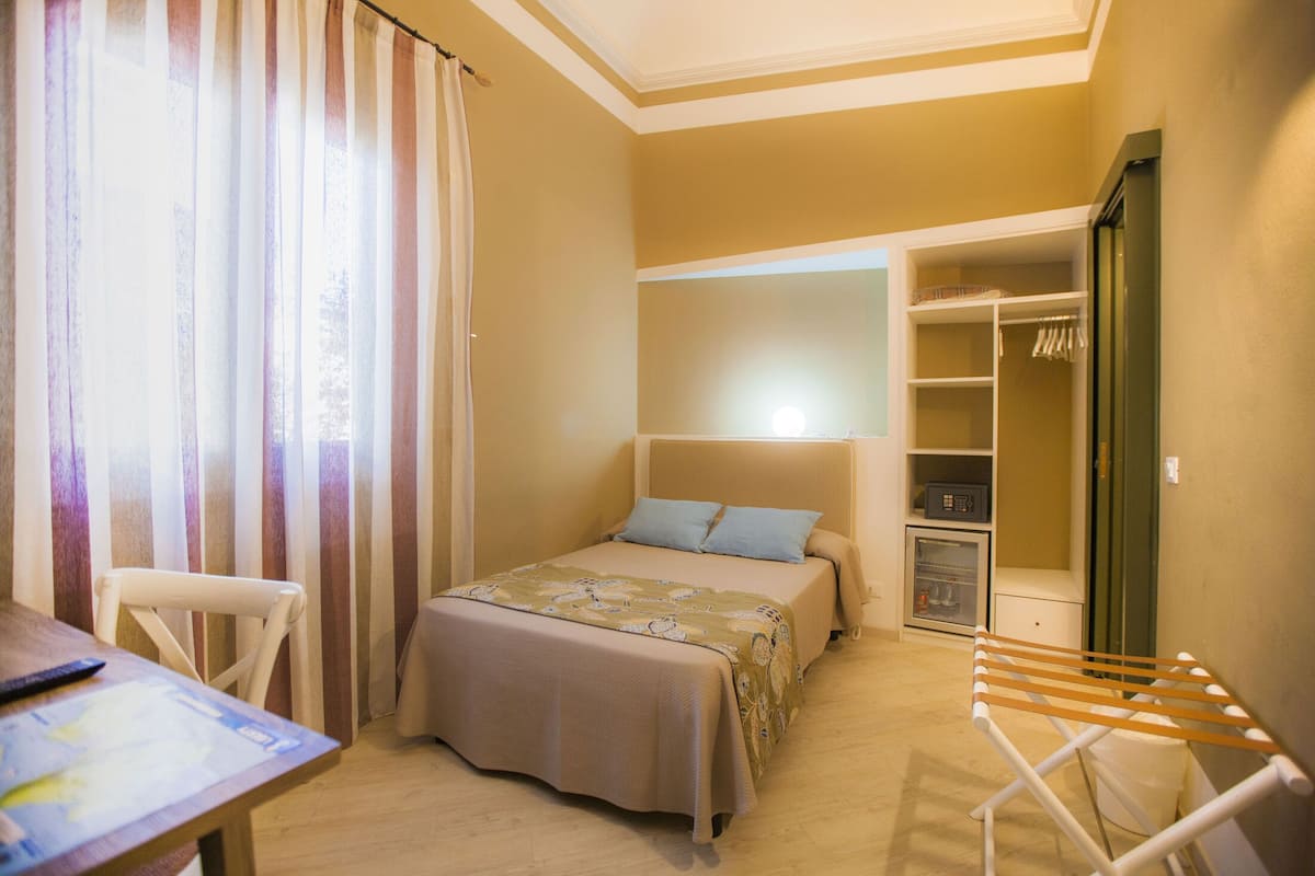 Una habitación pequeña con cama, silla, mesa, tendedero y armario.