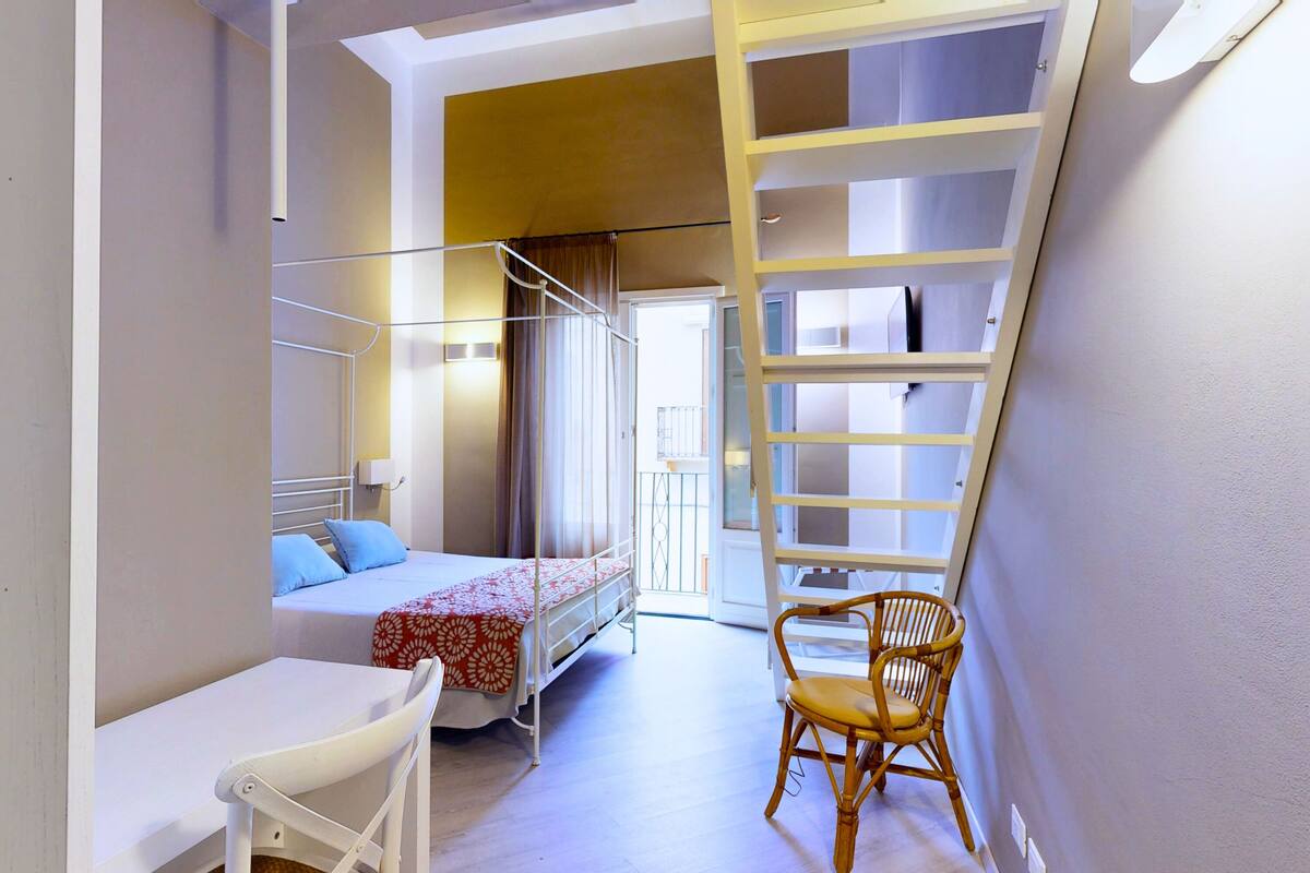 Una habitación pequeña con una cama litera, una mesita, una silla y una escalera que da a una zona superior.