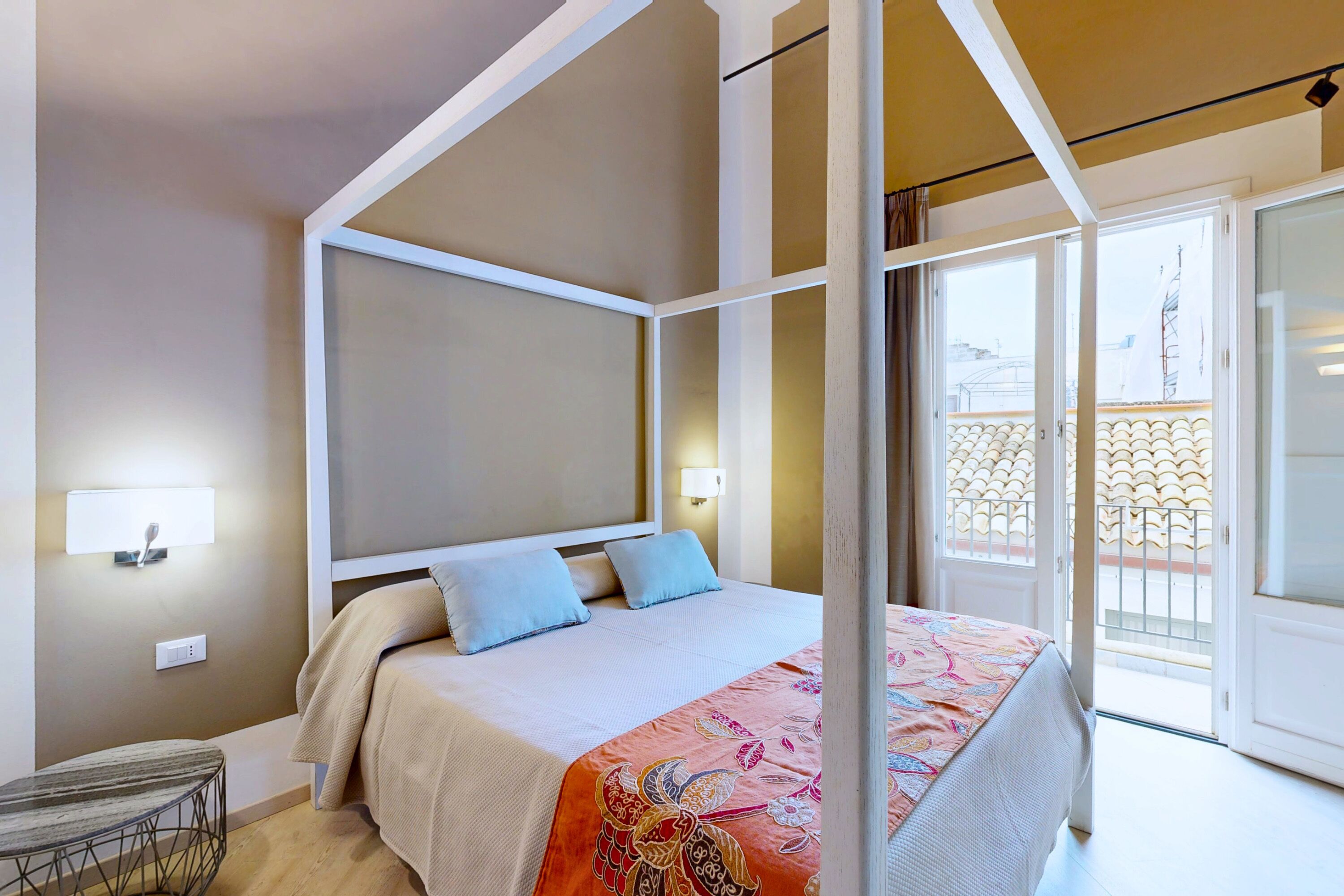 A bedroom with a four-poster bed, a bedside table, and a view of the outside balcony.
