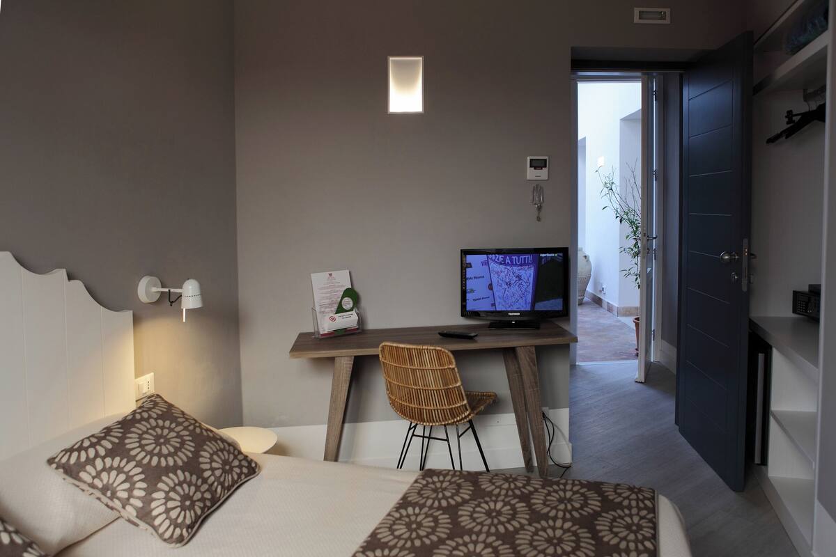 Habitación de hotel con cama, escritorio con computadora, una silla y puerta que da a un balcón.