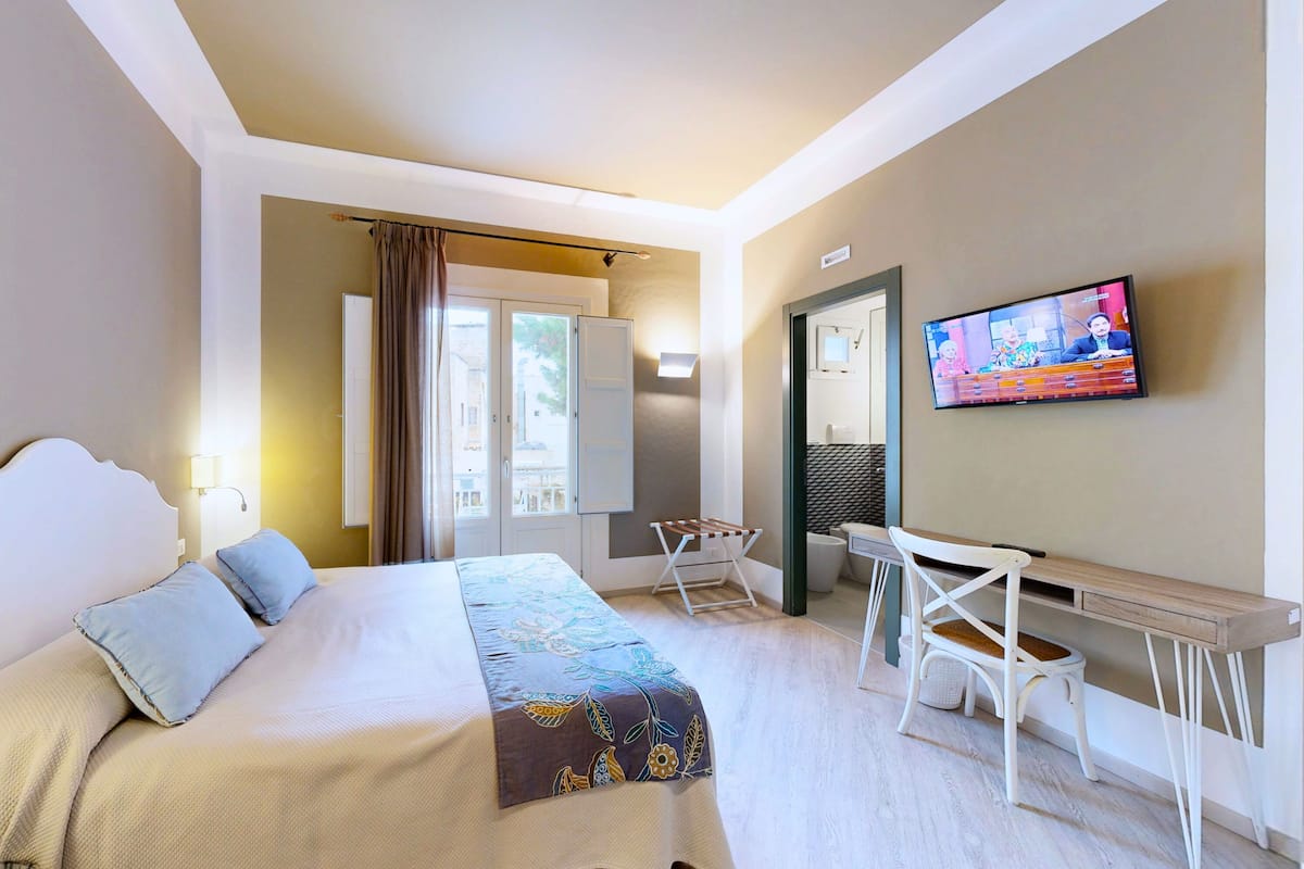Habitación de hotel con cama, escritorio, televisión y vistas al exterior.