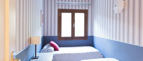 A room with two beds, a wooden dresser, a lamp, and a window with blinds.