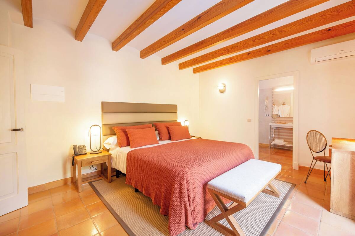 Une chambre à coucher avec un grand lit, des tables de chevet, un banc et un miroir.